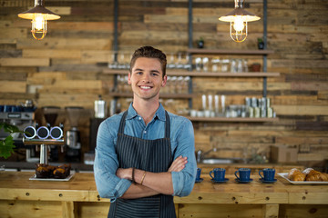 Portrait of smiling waiter standing with arms crossed - obrazy, fototapety, plakaty