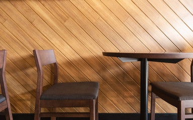 Wooden chairs and table beside with diagonal line of laminate wood wall. Light shining from corner...