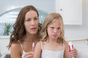 Mother and displeased daughter with toothbrush and toothpaste