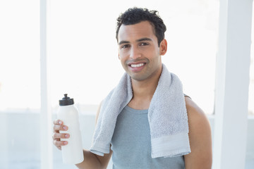 Man with towel around neck holding water bottle in fitness studio