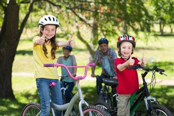 Happy family on their bike at the park with thumbs up 