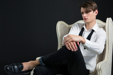 Androgynous man sitting on chair against black background