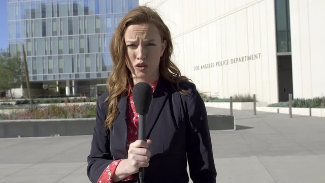 MS smartly dressed female TV reporter talks with microphone in front of Los Angeles Police Department headquarters in Downtown Los Angeles. Hand-held, stabilized, real time 4K UHD. Mute