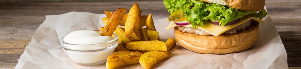 Banner of Home made hamburger with chicken, onion, cucumber, lettuce and cheese on wooden table with potato fries