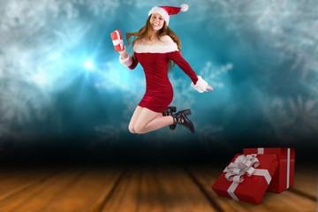 Fototapeta na wymiar Festive redhead jumping with gift against shimmering light design over boards