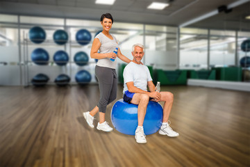 Full length portrait of a happy fit couple against large empty fitness studio with shelf of exercise balls