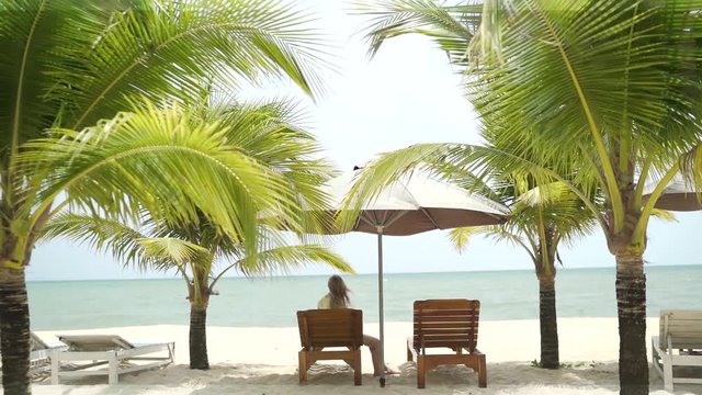  A beautiful girl in a swimsuit lies on a lounger under the malmas. A girl is resting by the sea. The girl is lying on the deckchair. Girl under the palm trees.