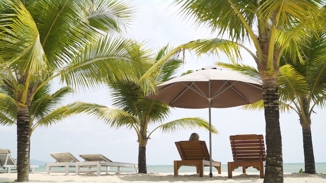  A beautiful girl in a swimsuit lies on a lounger under the malmas. A girl is resting by the sea. The girl is lying on the deckchair. Girl under the palm trees.