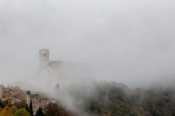 Fototapeta na wymiar View of St. Francis papal church in Assisi (Umbria, Italy) in the middle of lifting morning fog