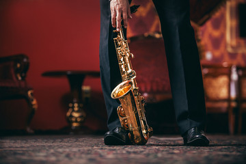 man in trousers holds a saxophone with his hand in the room