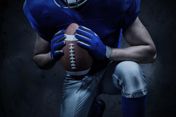 Fototapeta na wymiar Mid section of American football player kneeling while holding ball against orange background
