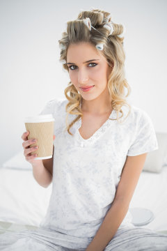 Peaceful pretty blonde wearing hair curlers holding coffee
