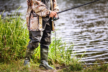 a man in military uniform and rubber boots is fishing on the river bank