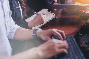 Businessman typing text on laptop computer and female secretary is recording a meeting by short note in business meeting in office