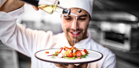 Handsome chef pouring olive oil on meal in a commercial kitchen