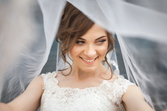 Portrait of beautiful, young smiling bride with white veil over her face. Concept of young gorgeous bride.