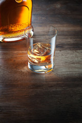 view of glass of  whiskey and a bottle aside on color background. 