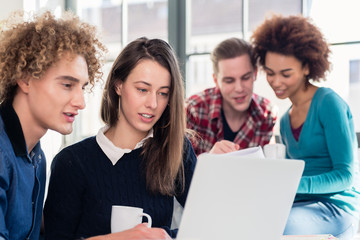 Two young students searching for an answer to their question both online and in a textbook while sitting at desk in the classroom during break