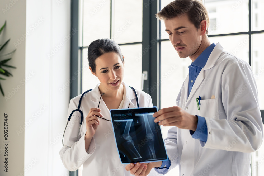 Wall mural two young dedicated doctors analyzing together the radiograph of the leg of a patient in a modern ho