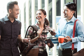 Three young and cheerful employees wearing trendy casual clothes while talking together in the morning in a modern workplace 