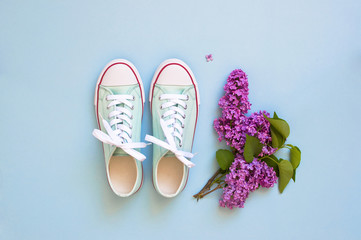 Pastel turquoise female sneakers and lilac flowers on blue background. Flat lay, top view minimal background. Fashion blog or magazine concept.