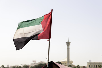 The UAE flag, flying the breeze, on Dubai Creek with the old district of Dubai, Bur Dubai, and a mosque minaret, in the background 