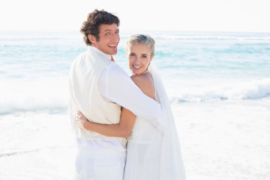 Newlyweds standing by the sea smiling at camera