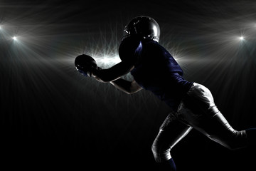 Silhouette American football player catching ball against spotlight