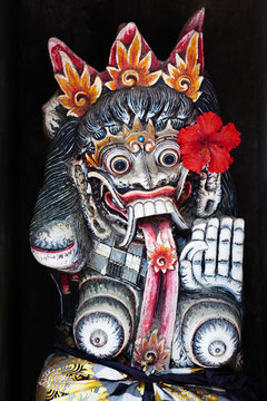 Old figure of traditional Balinese hindu spirit Rangda on wall of village temple at Bali island. Decorated by red flower for religious festival at Galungan holiday. Art, culture of Indonesian people.