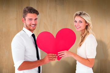 Attractive young couple holding red heart against wooden planks