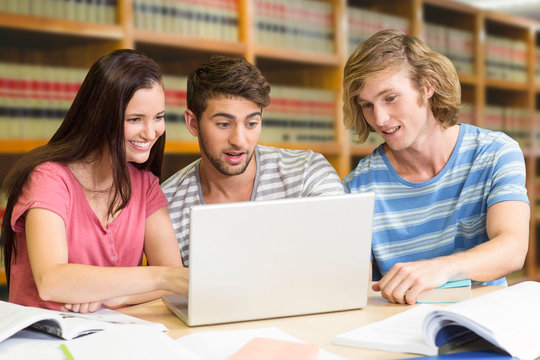 College students using laptop in library against close up of a bookshelf