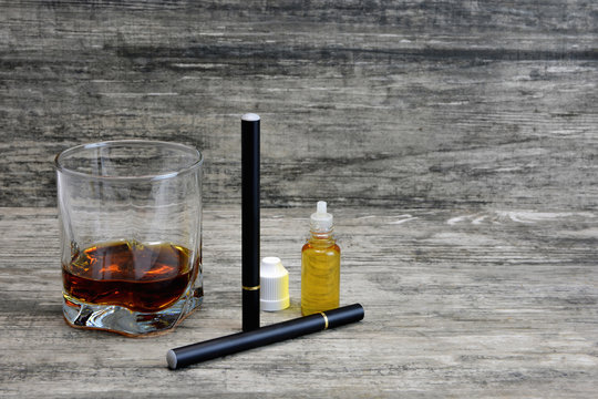 Whiskey in a glass with an e-cigarette and liquid for it on a gray stone background
