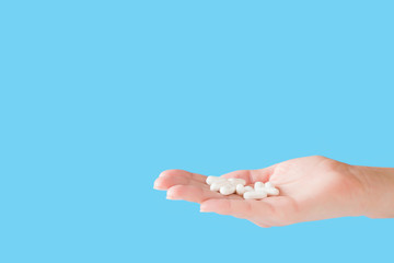 White pills in woman's hand. Receiving vitamins or medicaments. Medical, pharmacy and healthcare concept. Copy space. Empty place for text or logo on blue background.