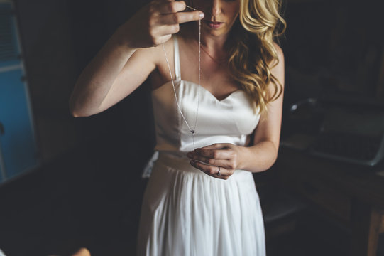 Blonde bride putting on a necklace bridal jewelry