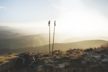 Ascent into the mountains, nordic walking sticks and a backpack, a traveler's set. Wonderful sunset in the background - obrazy, fototapety, plakaty