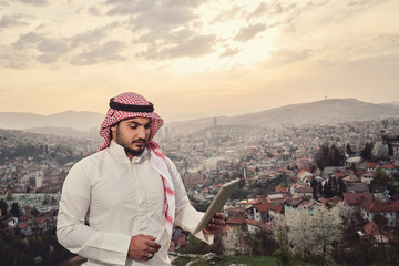 Handsome Arabic guy holding tablet. City view