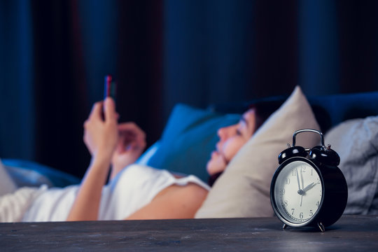 Photo of woman with insomnia with phone in hands lying on bed in bedroom