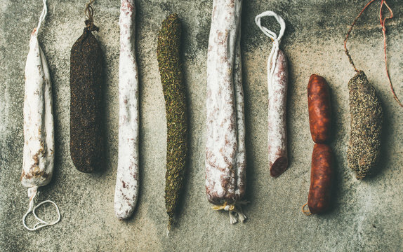 Variety of Spanish or Italian cured meat sausages. Flat-lay of fuets and salamies over rough grey concrete background, top view