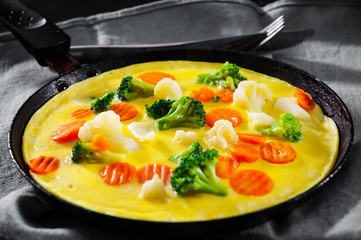 omelet with Mixed vegetables. cauliflower, broccoli and carrots in a frying pan on wooden table