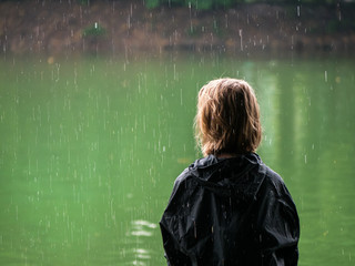 Mädchen im Regen sitzt auf einer bank und schaut auf den See