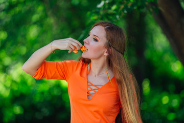Fototapeta premium Portrait of pretty red hair woman with juicy delicious orange at summer green park.