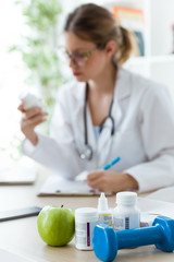 Female dietician holding a nutritional supplement while writing the properties in the consultation.