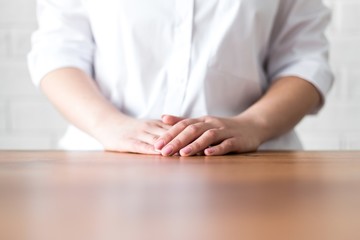 Girl folded her hands on a wooden table closeup