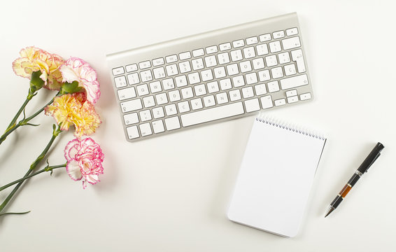 Background of white and pink flowers, yellow flowers, empty notebook next to pen and computer keyboard on white background. Copy space. Mockup.