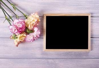Flowers of various colors next to blackboard on wooden table. Mockup.