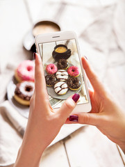 Woman photographing breakfast with coffee and donuts. Taking food photo with mobile phone.