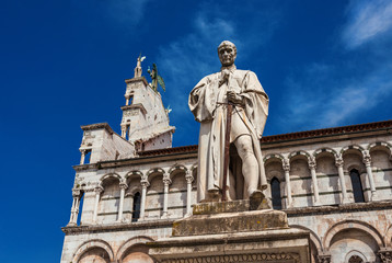Fototapeta na wymiar Francesco Burlamacchi monument erected in 1863 in the historic center of Lucca, with ancient Saint Michael in Foro Church in the backgorund