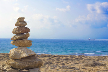 Fototapeta na wymiar Stones pyramid on background of Mediterranean sea. Seashore background with pile of stones. Tombs of Kings necropolis in Paphos, Cyprus