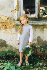 beautiful girl in a gray dress with a leaf in her hands standing on the grass against the background of the wall