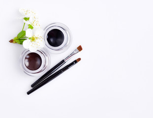 Makeup brushes and shadow for eyebrows with flowers on white background. Top view